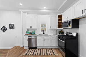 Kitchen with sink, white cabinets, light hardwood / wood-style floors, and appliances with stainless steel finishes