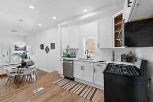 Kitchen featuring white cabinetry, sink, black range oven, light hardwood / wood-style flooring, and stainless steel dishwasher