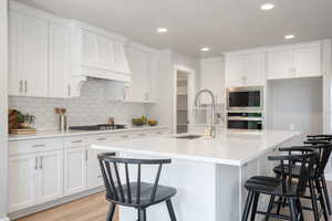 Kitchen featuring stainless steel appliances, a center island with sink, light hardwood / wood-style flooring, white cabinetry, and a breakfast bar area