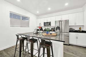 Kitchen featuring a breakfast bar area, white cabinetry, stainless steel appliances, and light wood-type flooring