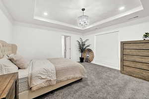 Bedroom featuring carpet flooring, a raised ceiling, and a notable chandelier