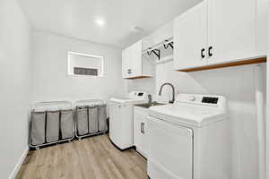 Clothes washing area featuring cabinets, separate washer and dryer, light hardwood / wood-style flooring, and sink