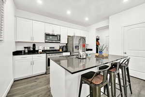 Kitchen featuring white cabinetry, stainless steel appliances, a kitchen breakfast bar, hardwood / wood-style floors, and a kitchen island with sink