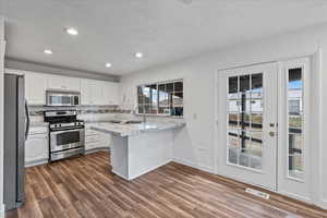 Kitchen with kitchen peninsula, backsplash, stainless steel appliances, wood-type flooring, and white cabinetry