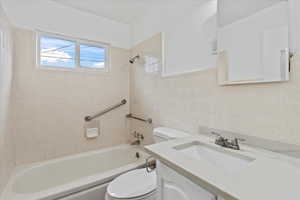 Full bathroom with toilet, vanity, tile walls, and tiled shower / bath