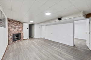 Basement with light hardwood / wood-style flooring, brick wall, and a brick fireplace