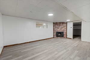 Basement with a brick fireplace and light hardwood / wood-style flooring