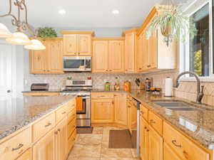 Kitchen with pendant lighting, backsplash, sink, light brown cabinetry, and stainless steel appliances