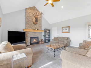 Living room featuring ceiling fan, a stone fireplace, carpet floors, and high vaulted ceiling