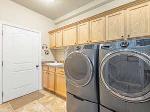 Clothes washing area featuring cabinets, sink, light tile patterned flooring, and washing machine and clothes dryer