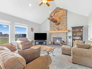 Carpeted living room with high vaulted ceiling, a stone fireplace, and ceiling fan