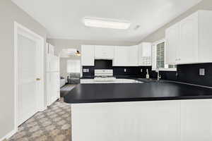 Kitchen featuring kitchen peninsula, sink, white cabinets, and white appliances