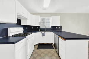 Kitchen featuring kitchen peninsula, stainless steel dishwasher, white range with gas cooktop, sink, and white cabinetry