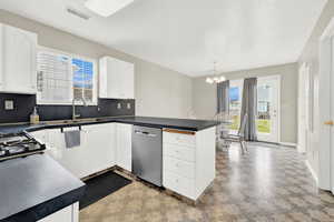 Kitchen featuring stainless steel dishwasher, sink, decorative light fixtures, white cabinets, and a chandelier