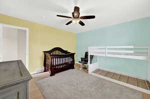 Bedroom featuring light wood-type flooring, a nursery area, and ceiling fan