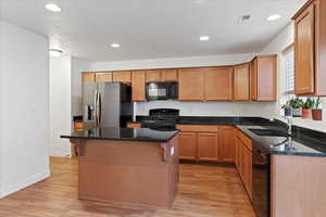 Kitchen featuring black appliances, a kitchen island, dark stone countertops, and light wood-type flooring