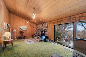 Living room with wooden ceiling, a wood stove, wooden walls, and vaulted ceiling