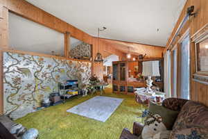 Carpeted living room featuring wood walls, vaulted ceiling, and a notable chandelier