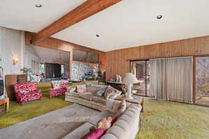 Carpeted living room featuring vaulted ceiling with beams and wooden walls