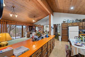 Kitchen with pendant lighting, lofted ceiling with beams, white refrigerator, and an inviting chandelier