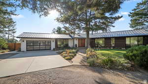 View of front of home featuring driveway, a standing seam roof, a garage, and a front yard