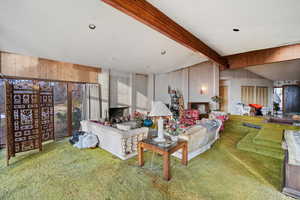 Living room with carpet flooring, lofted ceiling with beams, a fireplace, and wooden walls