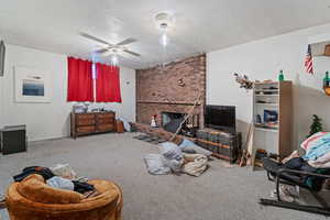 Carpeted living room featuring ceiling fan, a textured ceiling, and a brick fireplace