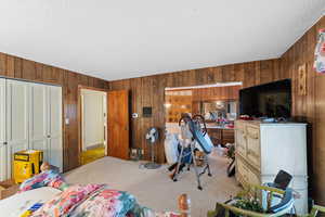 Carpeted bedroom with wood walls, a textured ceiling, and a closet