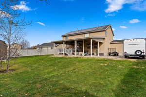 Rear view of property with a lawn, solar panels, and a patio area