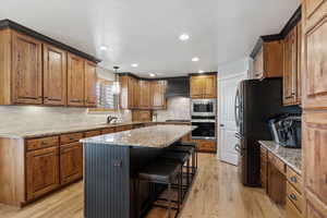 Kitchen featuring appliances with stainless steel finishes, light wood-type flooring, a center island, hanging light fixtures, and a breakfast bar area