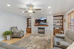 Living room with ceiling fan, a stone fireplace, and light hardwood / wood-style flooring