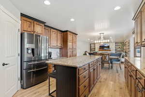 Kitchen featuring stainless steel fridge with ice dispenser, light hardwood / wood-style flooring, light stone counters, a kitchen bar, and a kitchen island