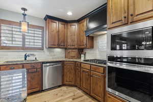 Kitchen with decorative backsplash, light stone counters, sink, and appliances with stainless steel finishes