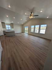 Unfurnished living room with plenty of natural light, ceiling fan, dark hardwood / wood-style flooring, and lofted ceiling