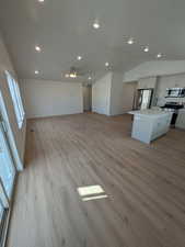 Unfurnished living room with ceiling fan, vaulted ceiling, and light hardwood / wood-style flooring