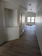 Hallway featuring dark hardwood / wood-style flooring, lofted ceiling, and a textured ceiling