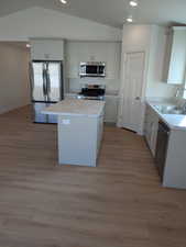 Kitchen with light hardwood / wood-style floors, sink, stainless steel appliances, and vaulted ceiling