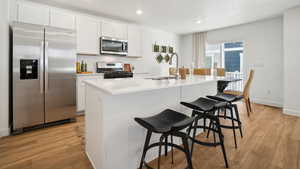 Kitchen with stainless steel appliances, a kitchen island with sink, sink, light hardwood / wood-style floors, and white cabinetry