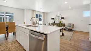 Kitchen with dishwasher, a kitchen island with sink, white cabinets, sink, and light hardwood / wood-style floors