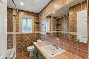 Full bathroom featuring tile patterned floors, vanity, tiled shower / bath combo, tile walls, and toilet