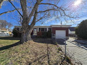 Single story home featuring a front lawn, driveway, fence, an attached garage, and brick siding