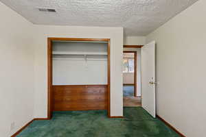 Unfurnished bedroom with dark colored carpet, a textured ceiling, and a closet