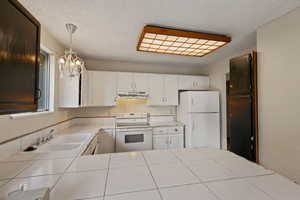 Kitchen featuring white cabinets, pendant lighting, white appliances, and sink