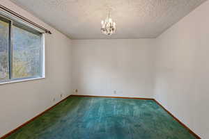 Carpeted spare room featuring a textured ceiling and a notable chandelier