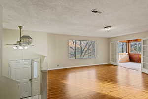 Unfurnished living room featuring ceiling fan, light hardwood / wood-style floors, a textured ceiling, and french doors