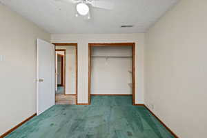 Unfurnished bedroom with carpet flooring, ceiling fan, a closet, and a textured ceiling