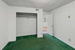 Unfurnished bedroom featuring a textured ceiling, dark carpet, and a closet