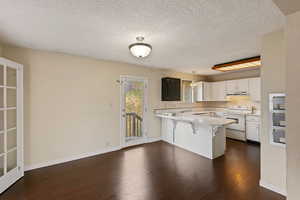 Kitchen featuring white cabinetry, dark hardwood / wood-style flooring, white range, kitchen peninsula, and a kitchen bar