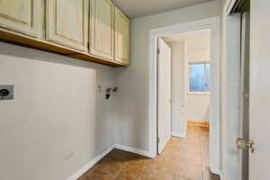 Washroom with cabinets, light tile patterned floors, hookup for a washing machine, and electric dryer hookup