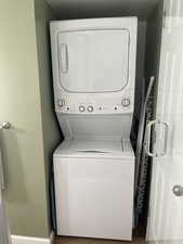 Clothes washing area featuring wood-type flooring and stacked washer and dryer